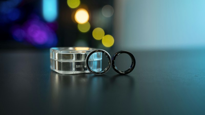 A smart health tracking ring shown next to its circular charging case