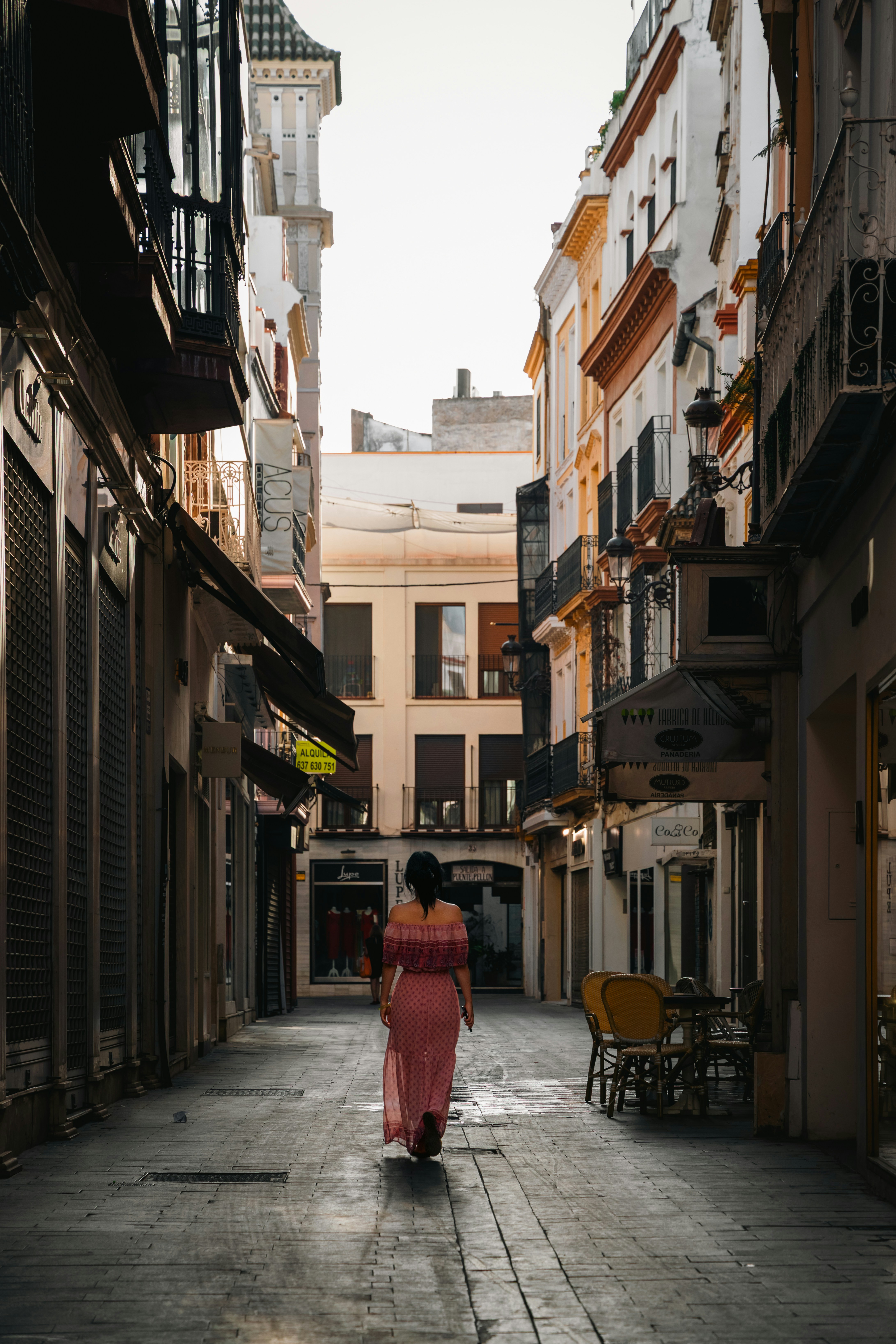 A woman walks down a narrow, cobblestone street.