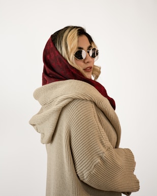 A woman poses wearing a headscarf and sweater.
