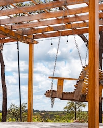 A wooden swing hangs under a pergola.