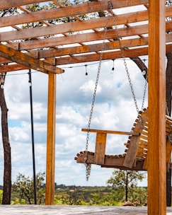 A wooden swing hangs under a pergola.