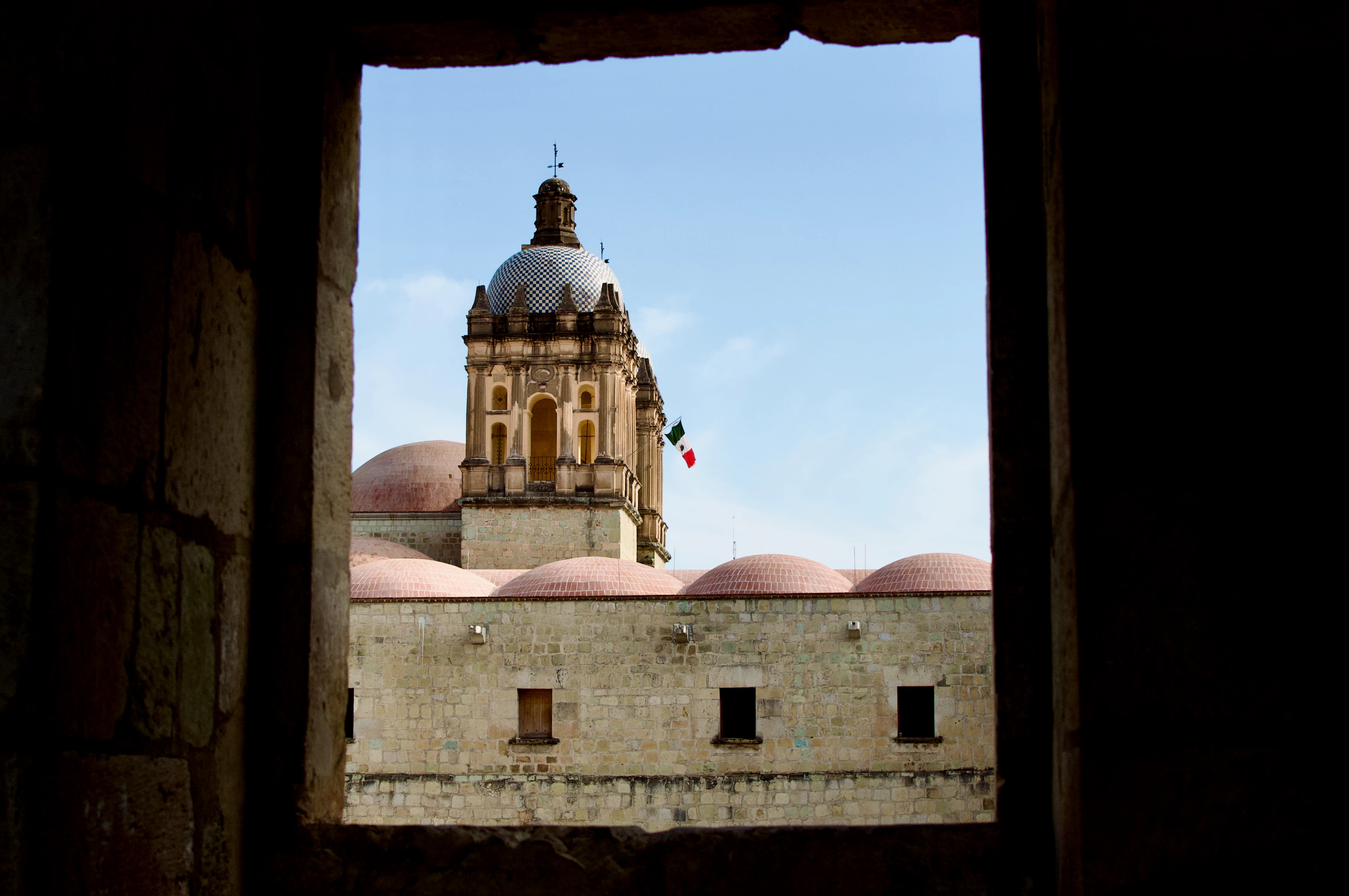 The tower and domes of the Church of Santo Domingo, framed by a dark stone window in Oaxaca