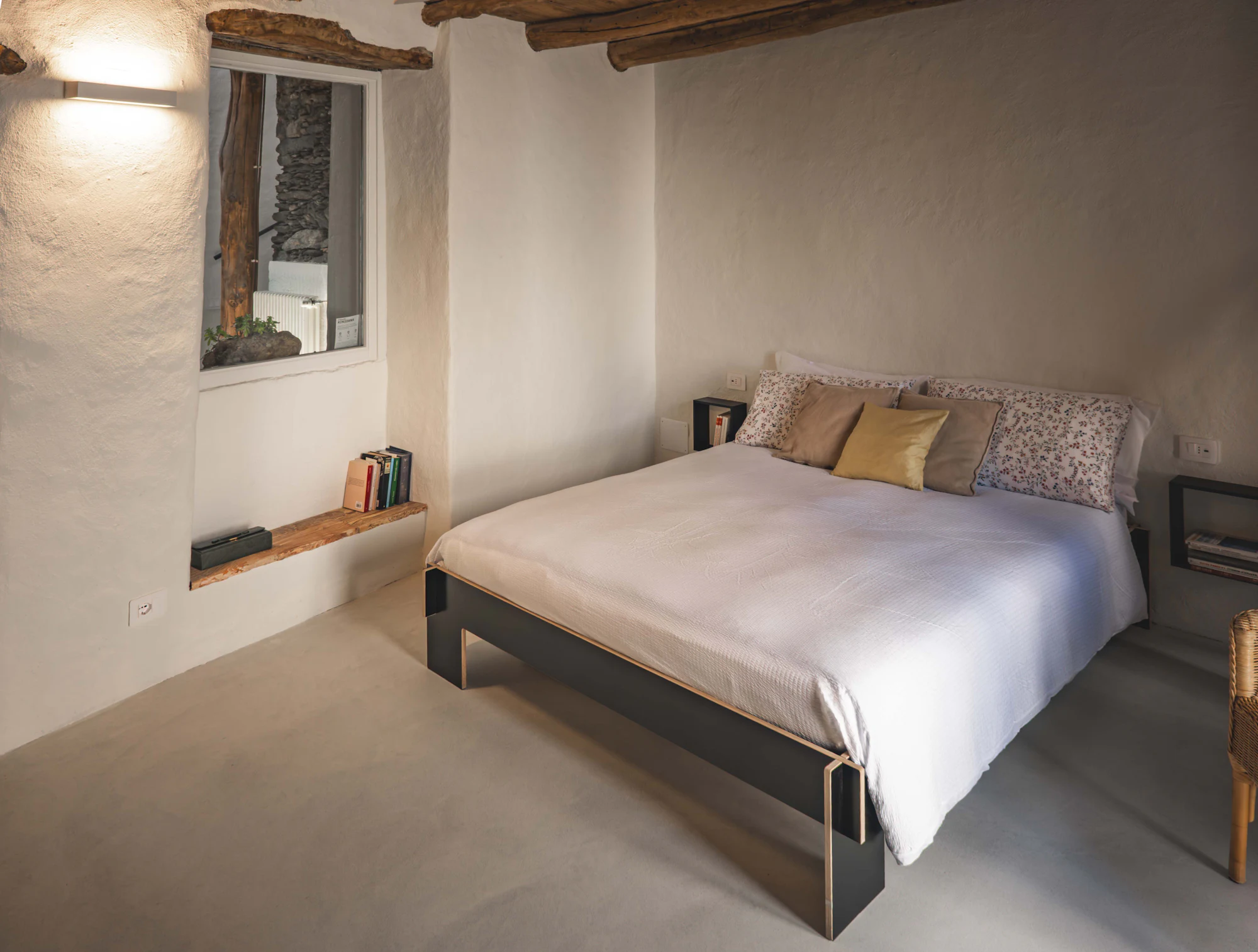 A whitewashed bedroom under old wooden beams with a deep-set window