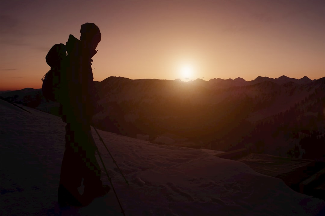 A person watches the sunset over snowy mountains.