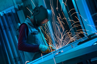 A welder works on metal, sparks flying.
