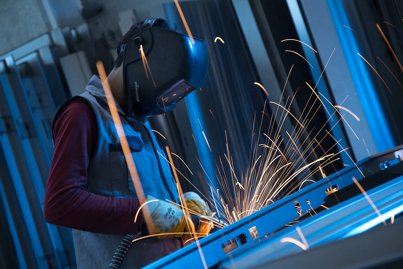 Un soldador con equipo de protección trabaja entre chispas en un taller industrial
