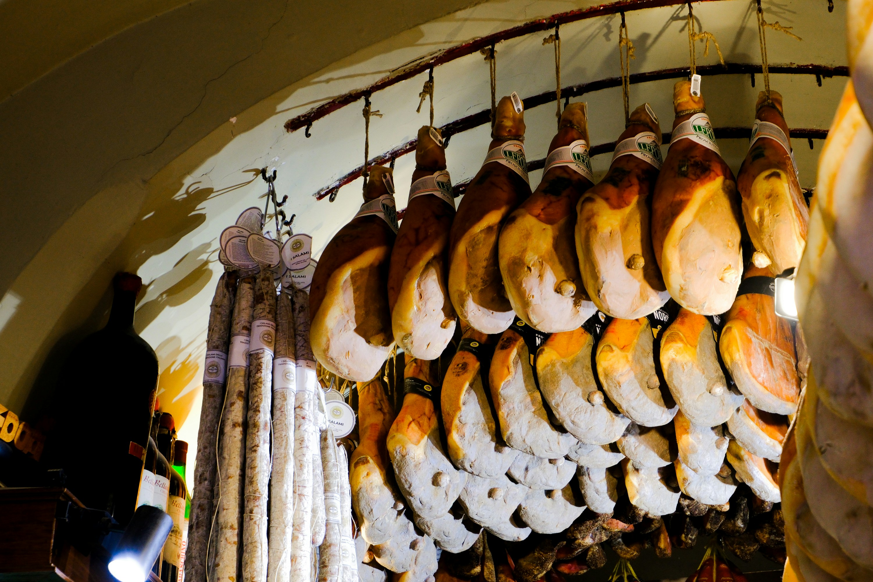 Hanging cured meats fill a dark, arched space.