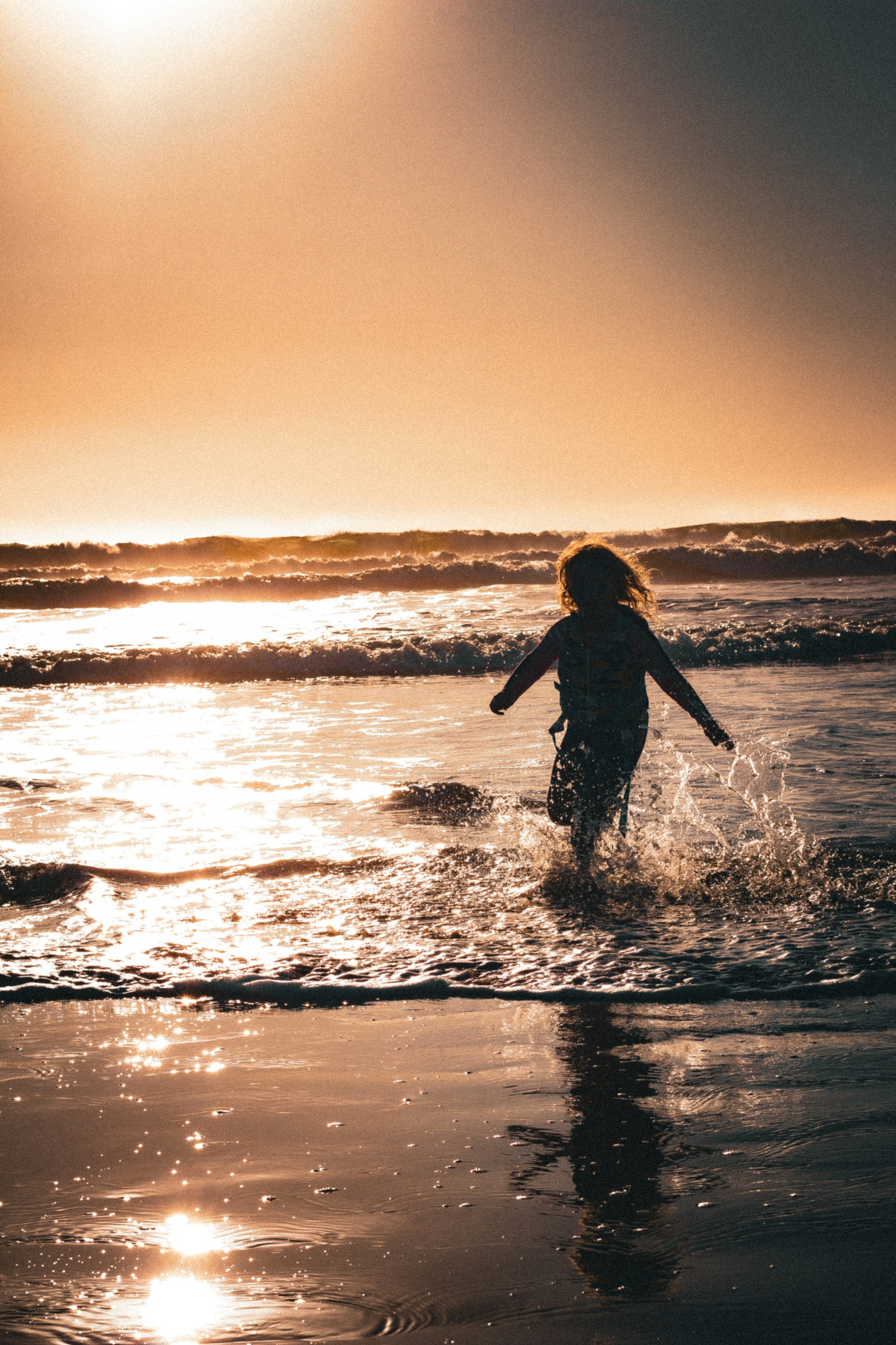 A child runs through the waves at sunset.