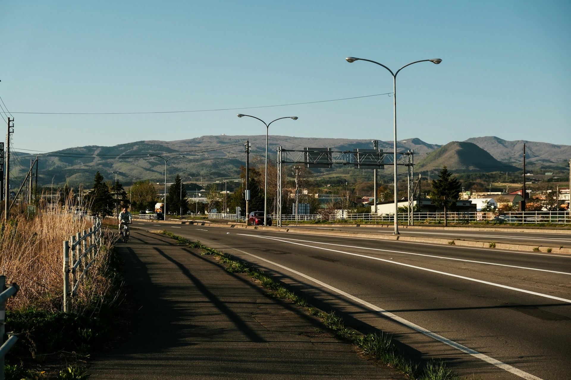 Road next to a grassy path and a mountain.