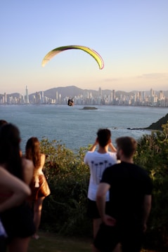 People watch a paraglider over the ocean and city.