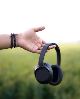 Hand holding a pair of black over-ear headphones.