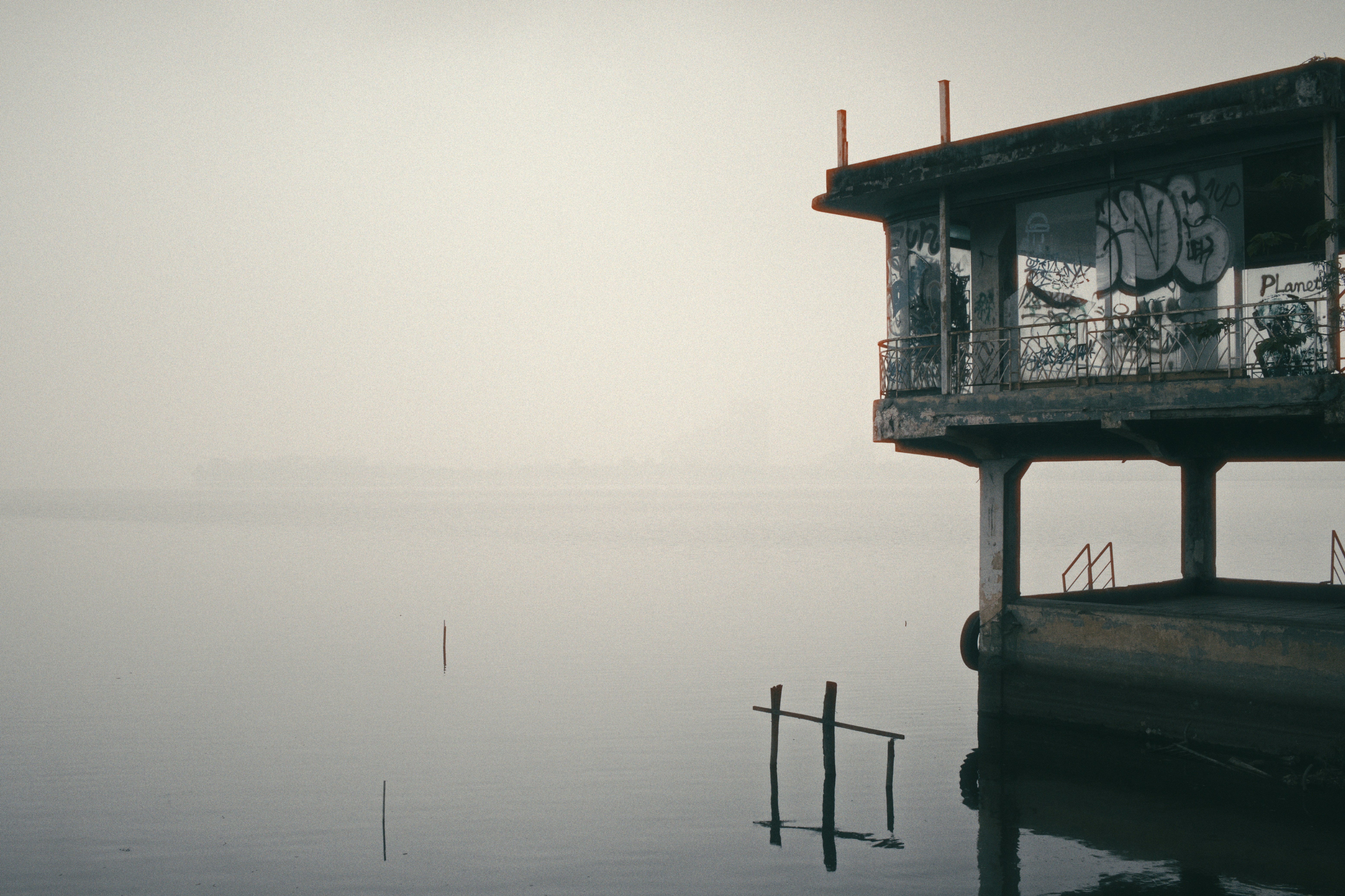 Abandoned structure stands over tranquil water.