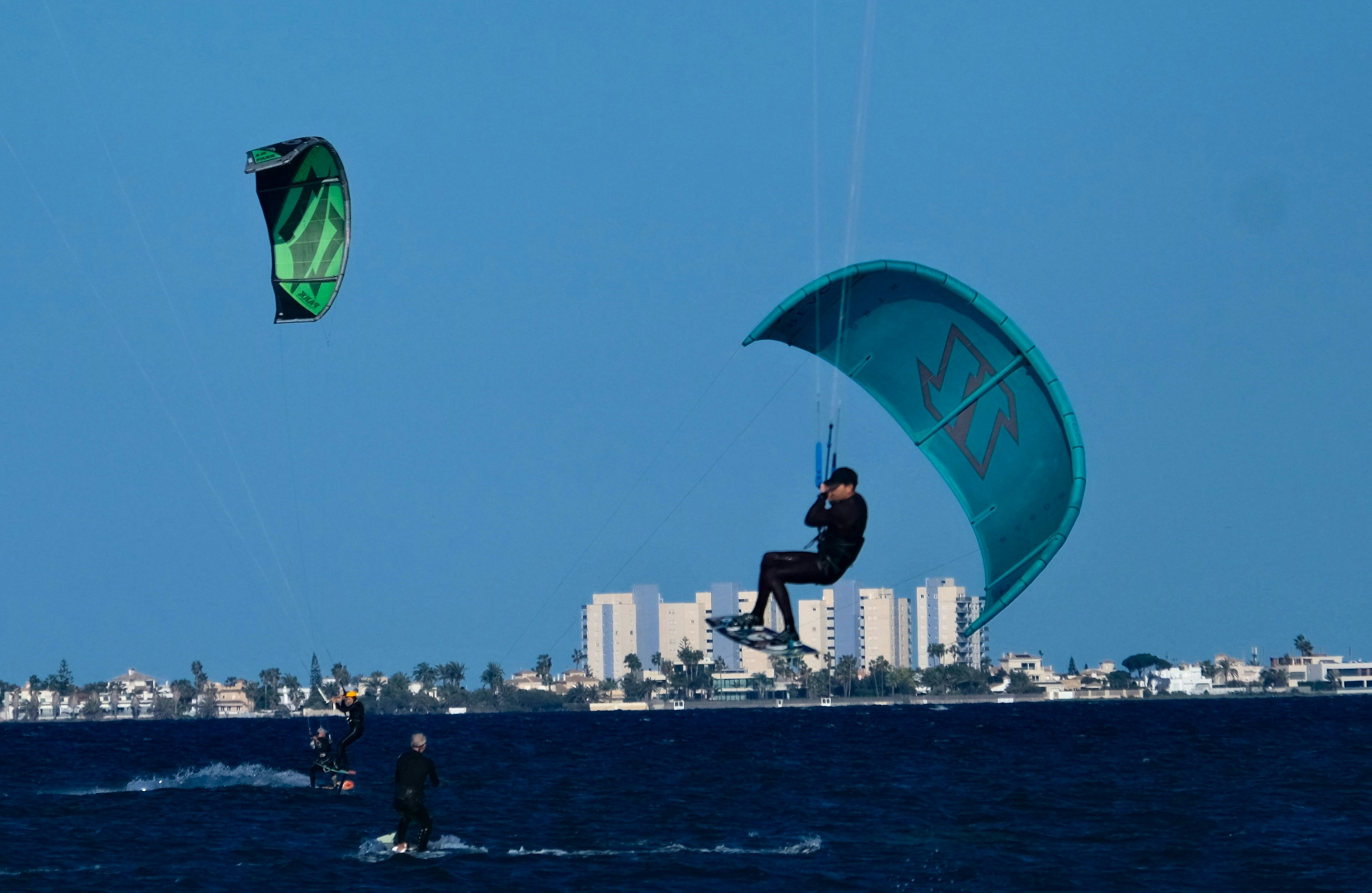 Kitesurfers glide across the water and soar in the sky.