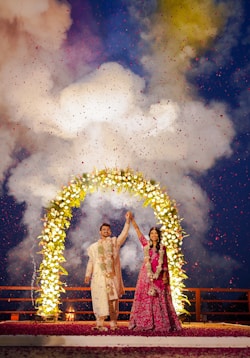 Couple celebrates under a floral arch with confetti.