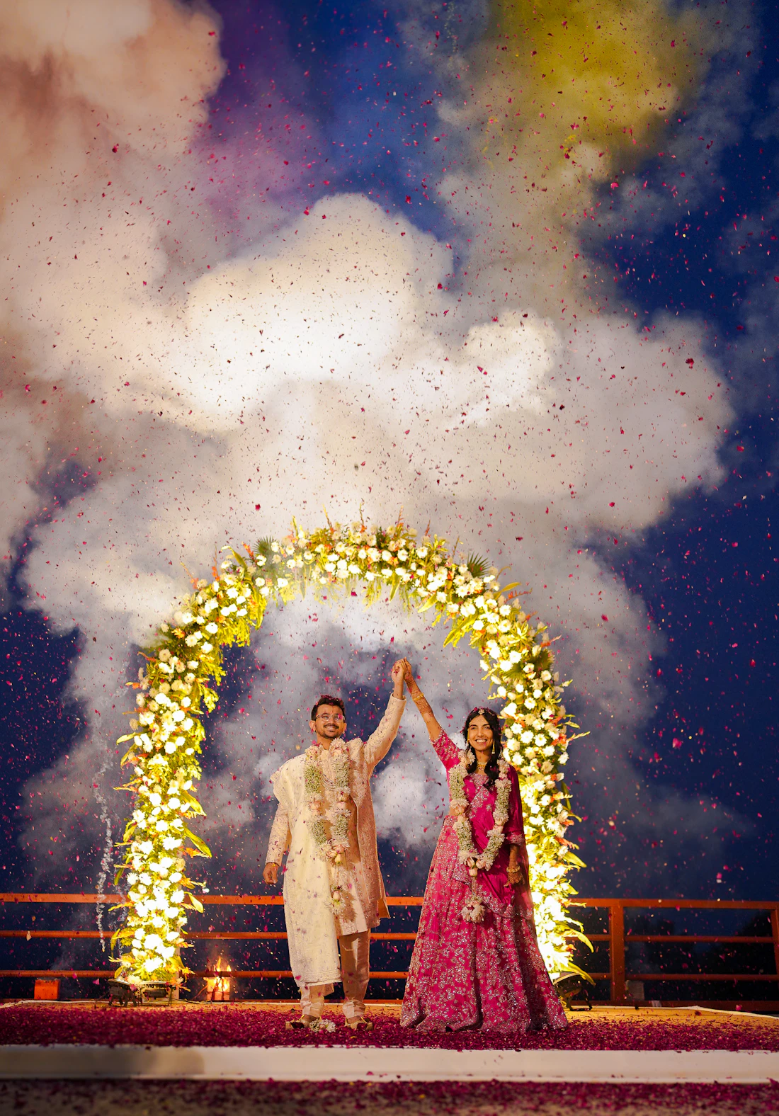 A couple celebrating under a floral arch with confetti
