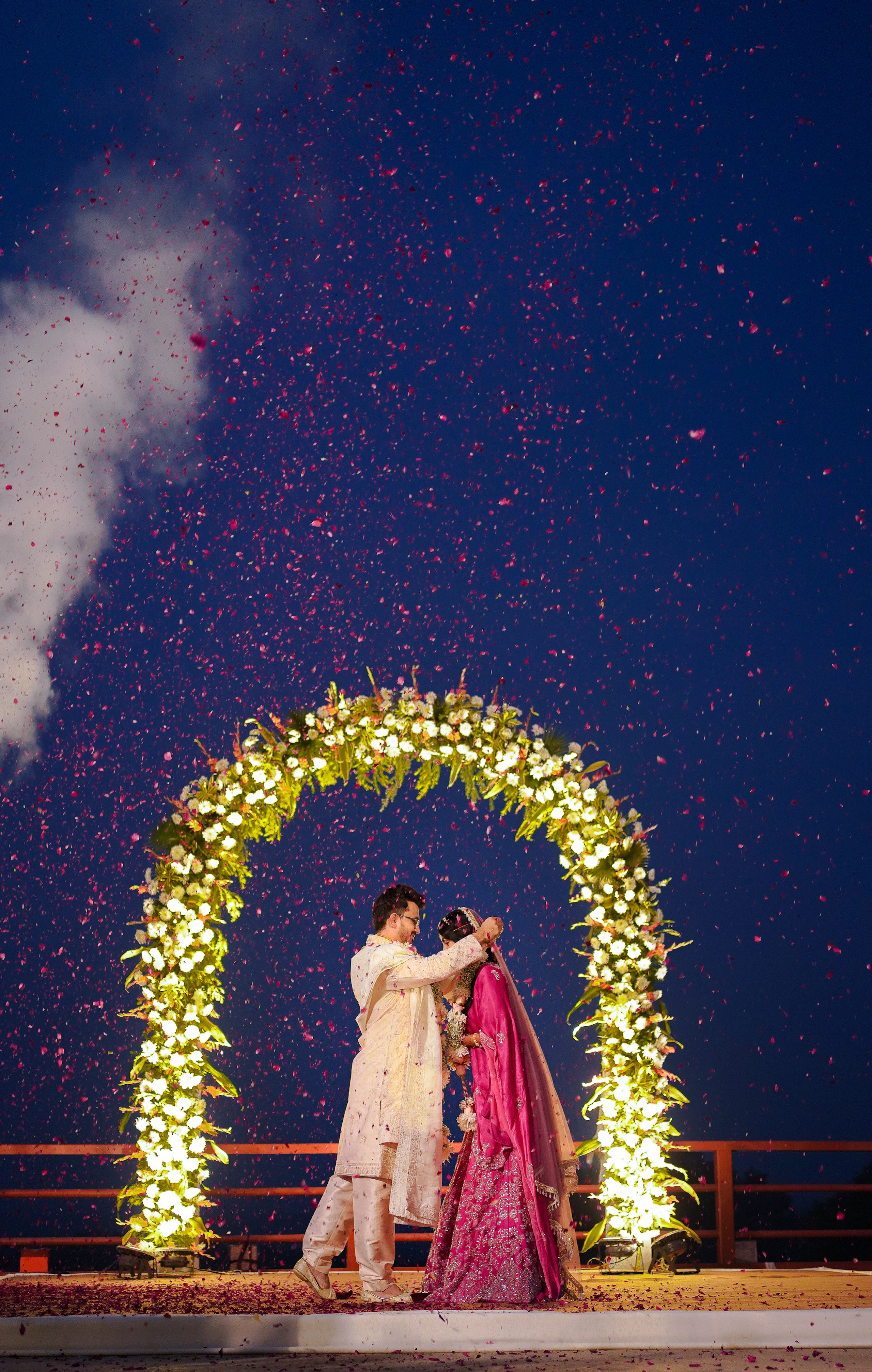 Couple exchanging vows beneath an illuminated flower archway at night