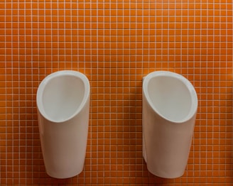 Two urinals hang against an orange tiled wall.
