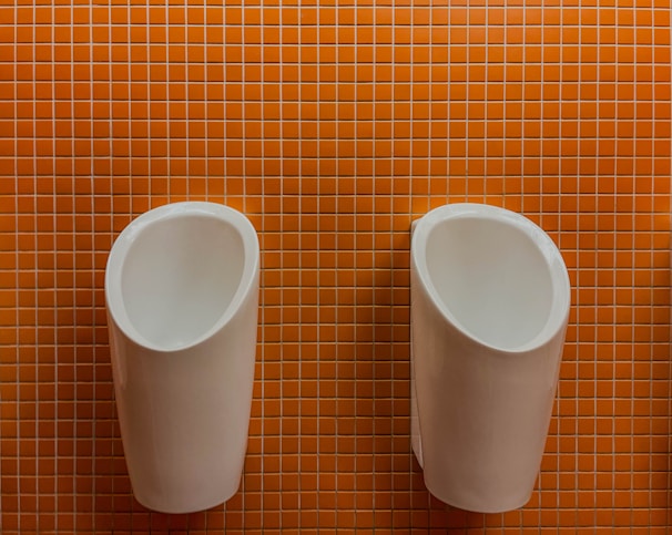 Two urinals hang against an orange tiled wall.