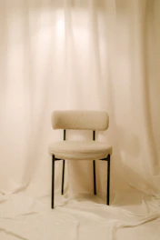 A single chair sits in front of white curtains.