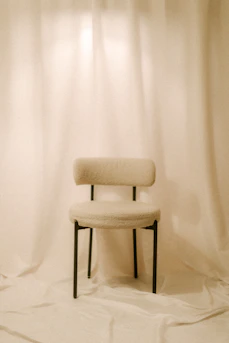 A single chair sits in front of white curtains.