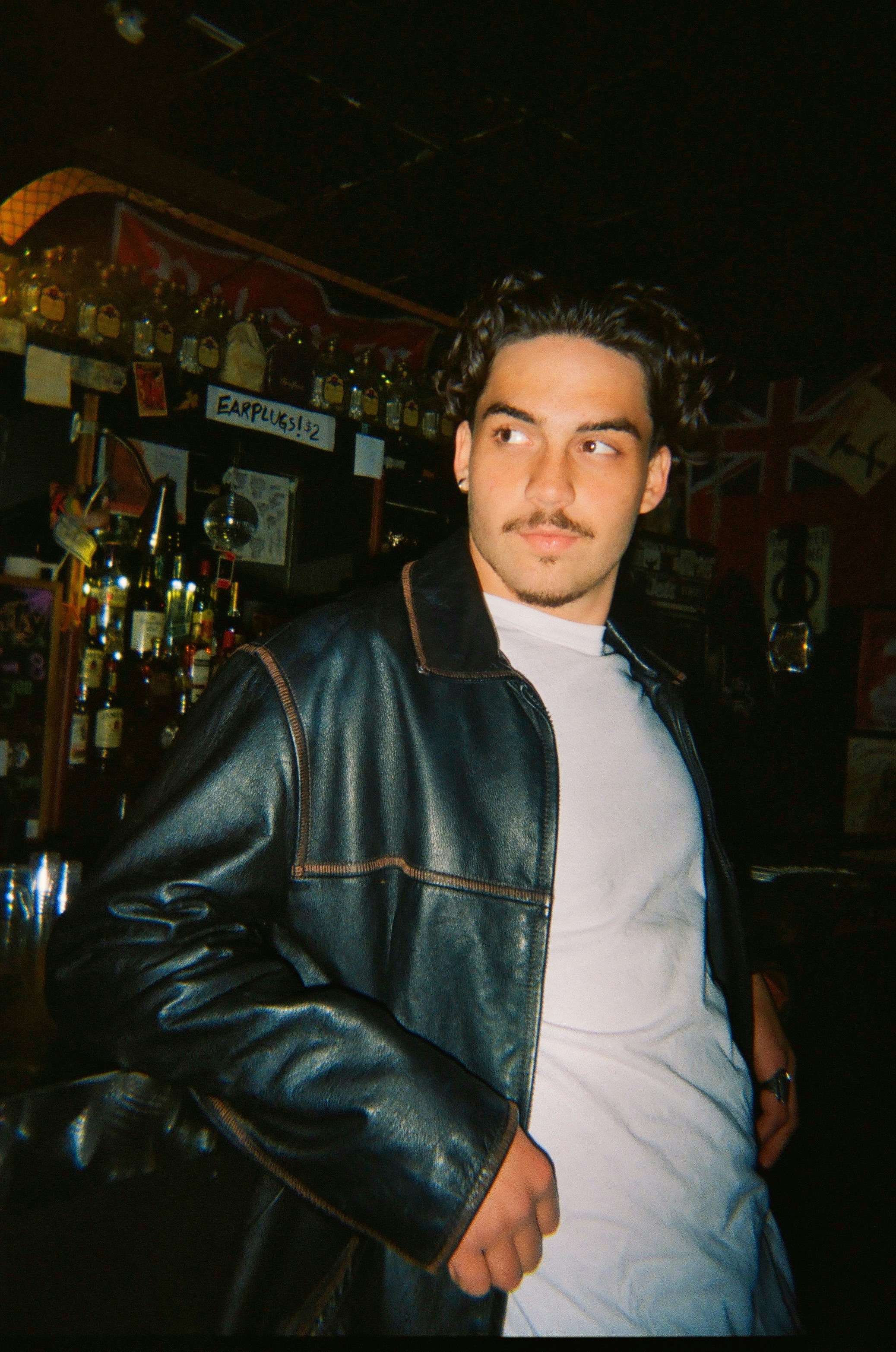 Man in a leather jacket and white tee in a bar