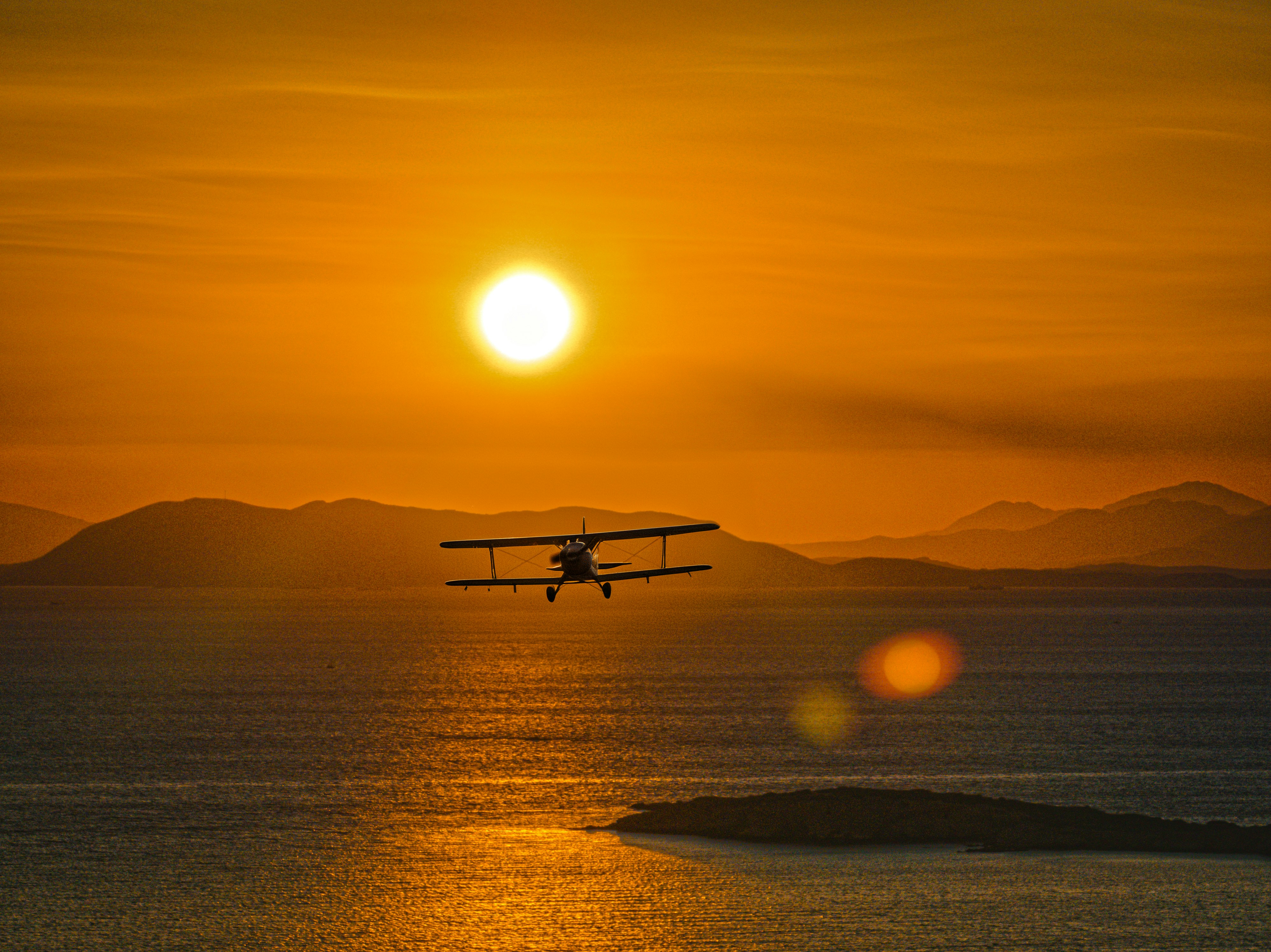 A plane flies into the sunset over the ocean.