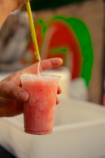 Person holds a plastic cup of a pink drink.