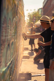 Youngsters are spray painting a mural outdoors.