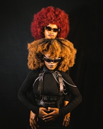 Two people with large afros and sunglasses pose.