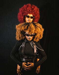Two people with large afros and sunglasses pose.