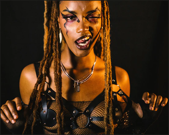 Woman with dreadlocks and artistic makeup poses.