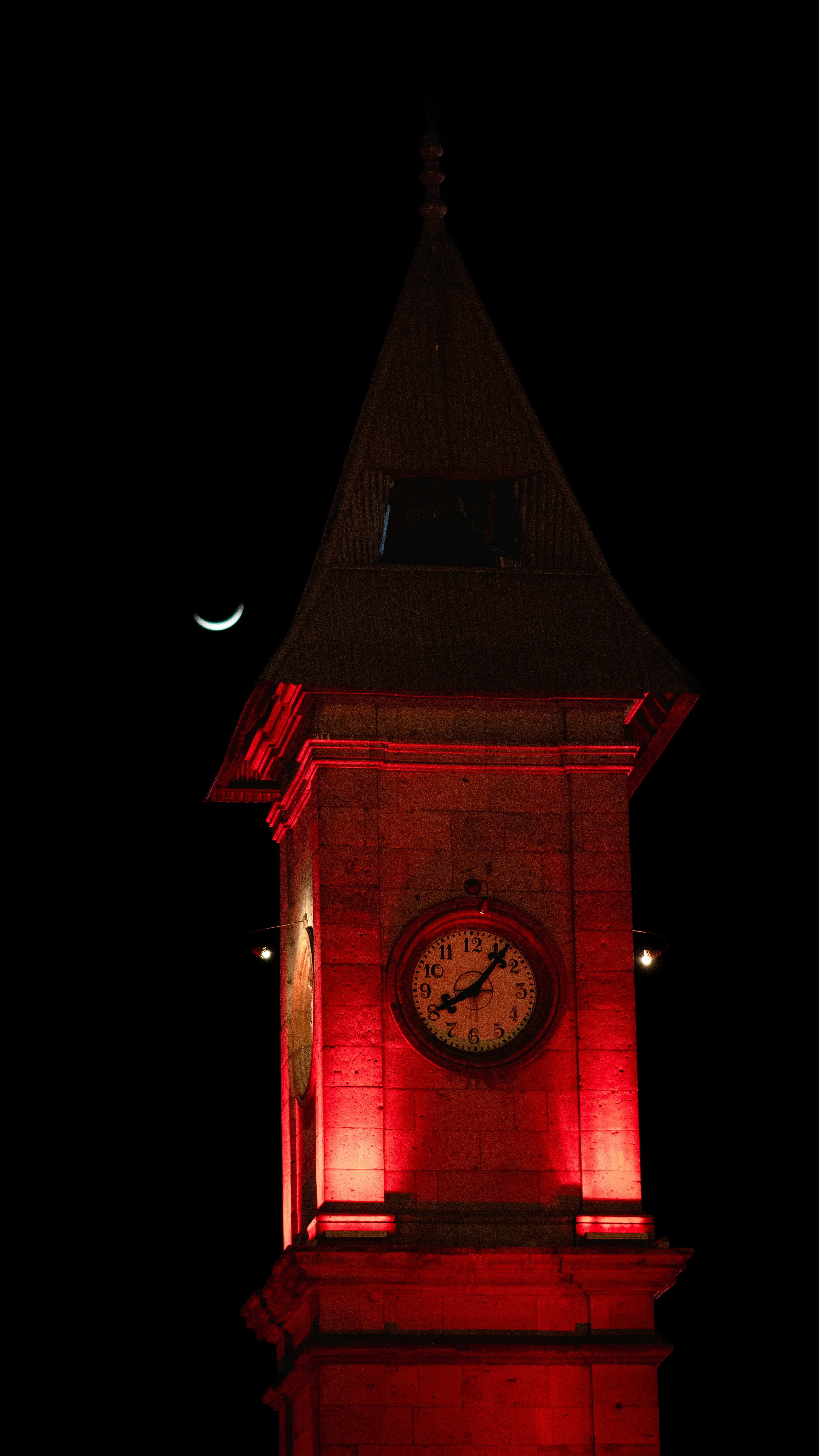 A red-lit clock tower against a black night sky.