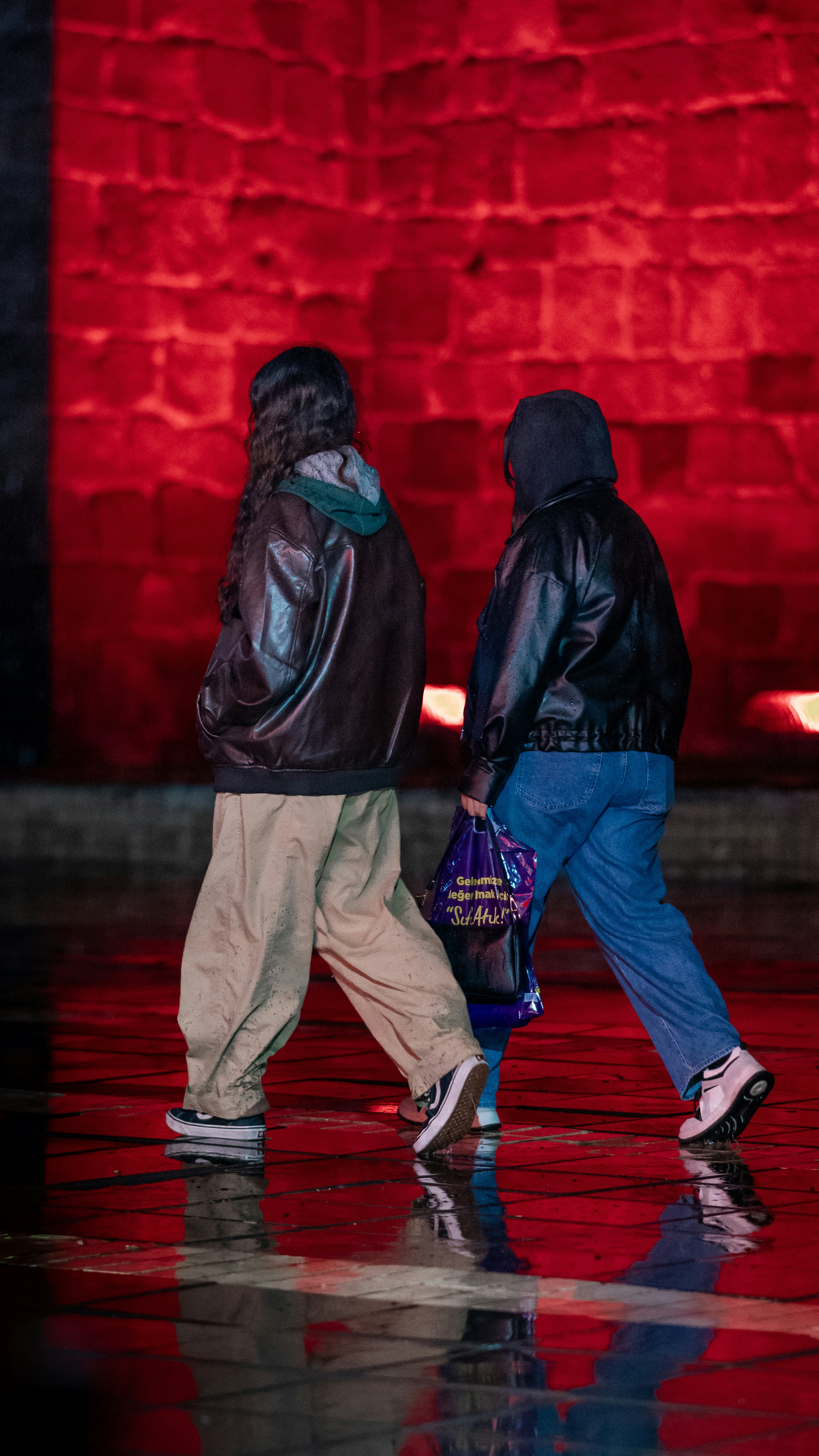 Two people walk on a wet street at night.