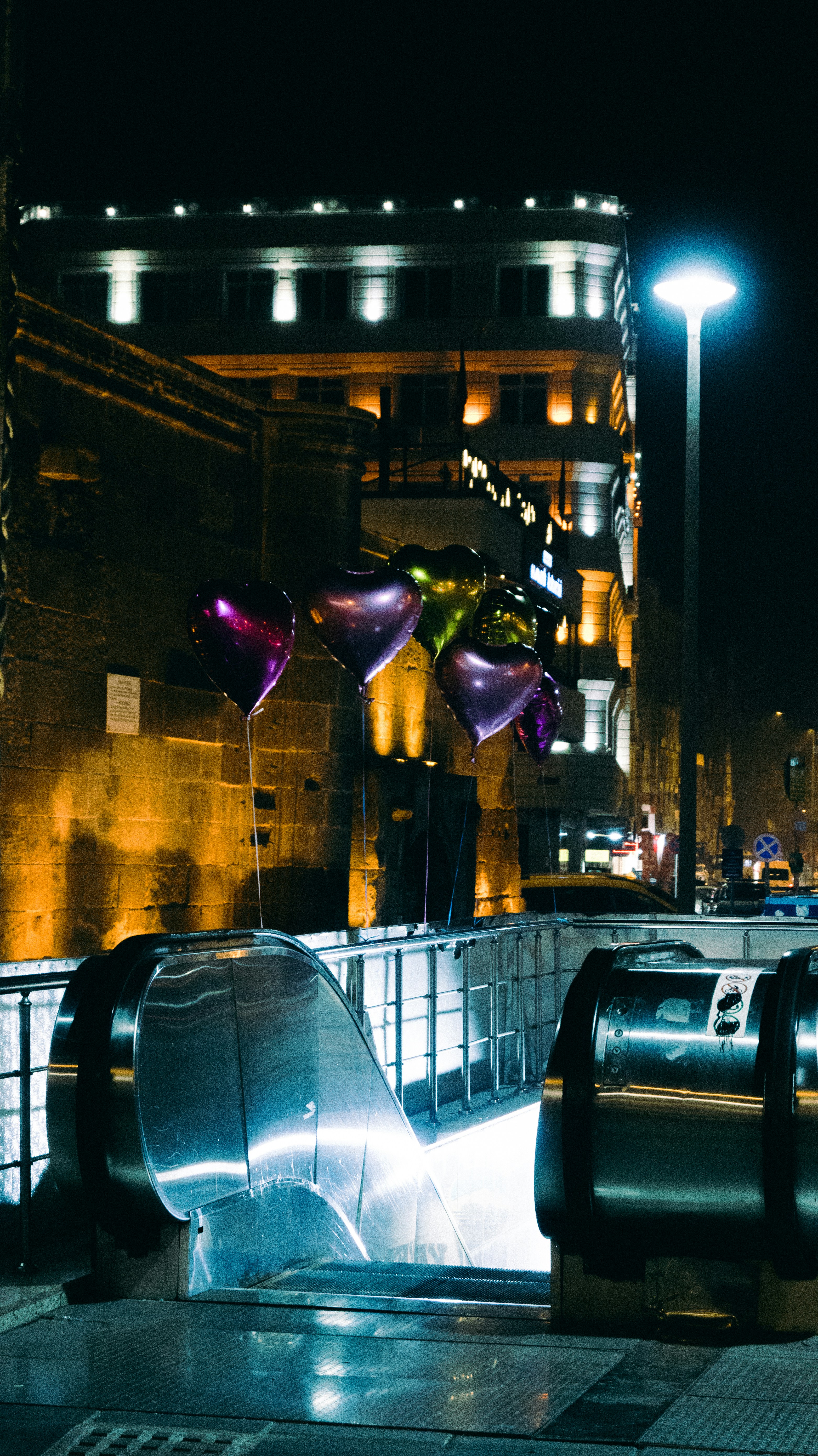 Heart-shaped balloons float above an escalator at night.