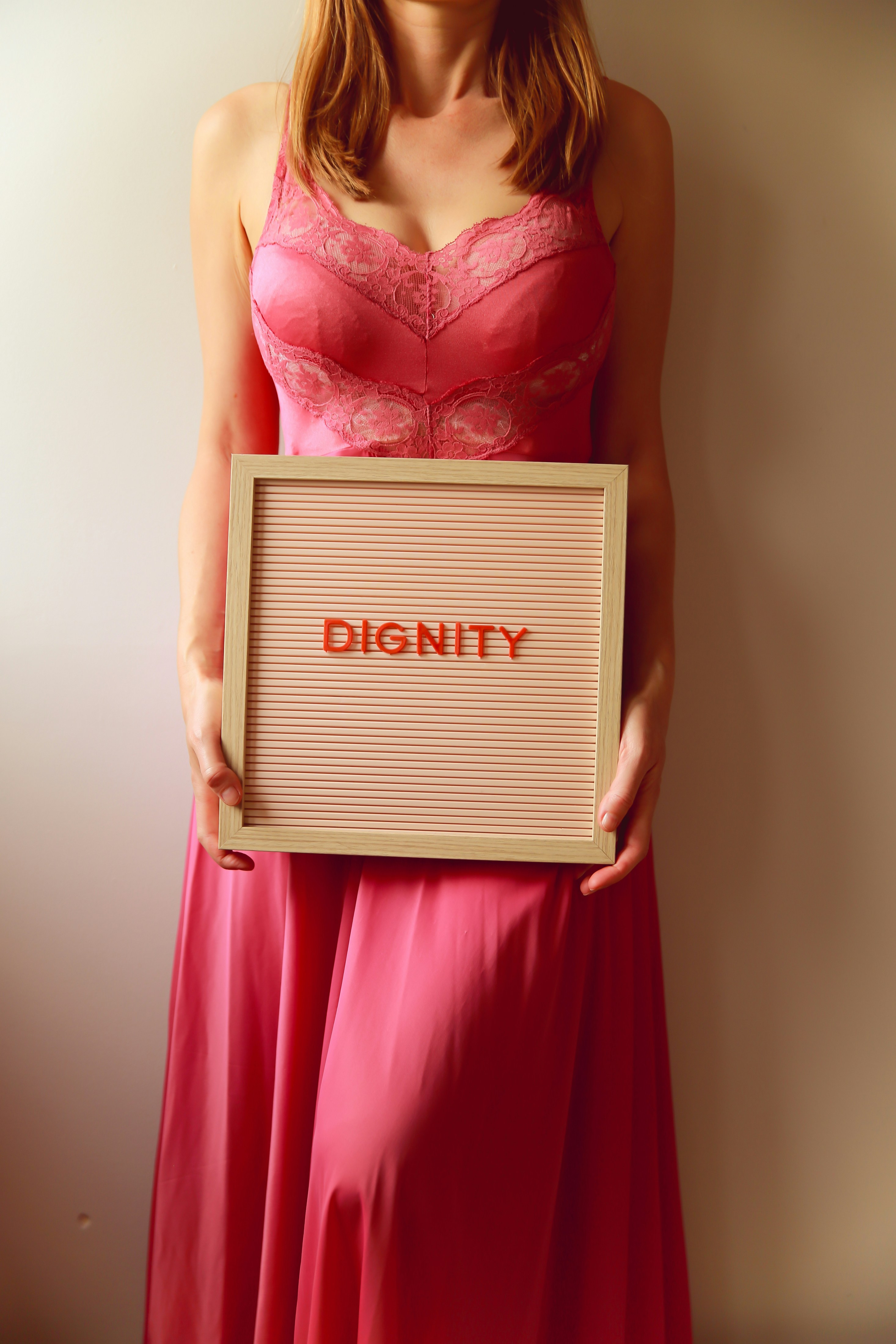 Frau in rosa Kleid hält Schild mit der Aufschrift "Würde".