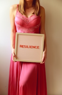 Woman in pink dress holds "resilience" sign.