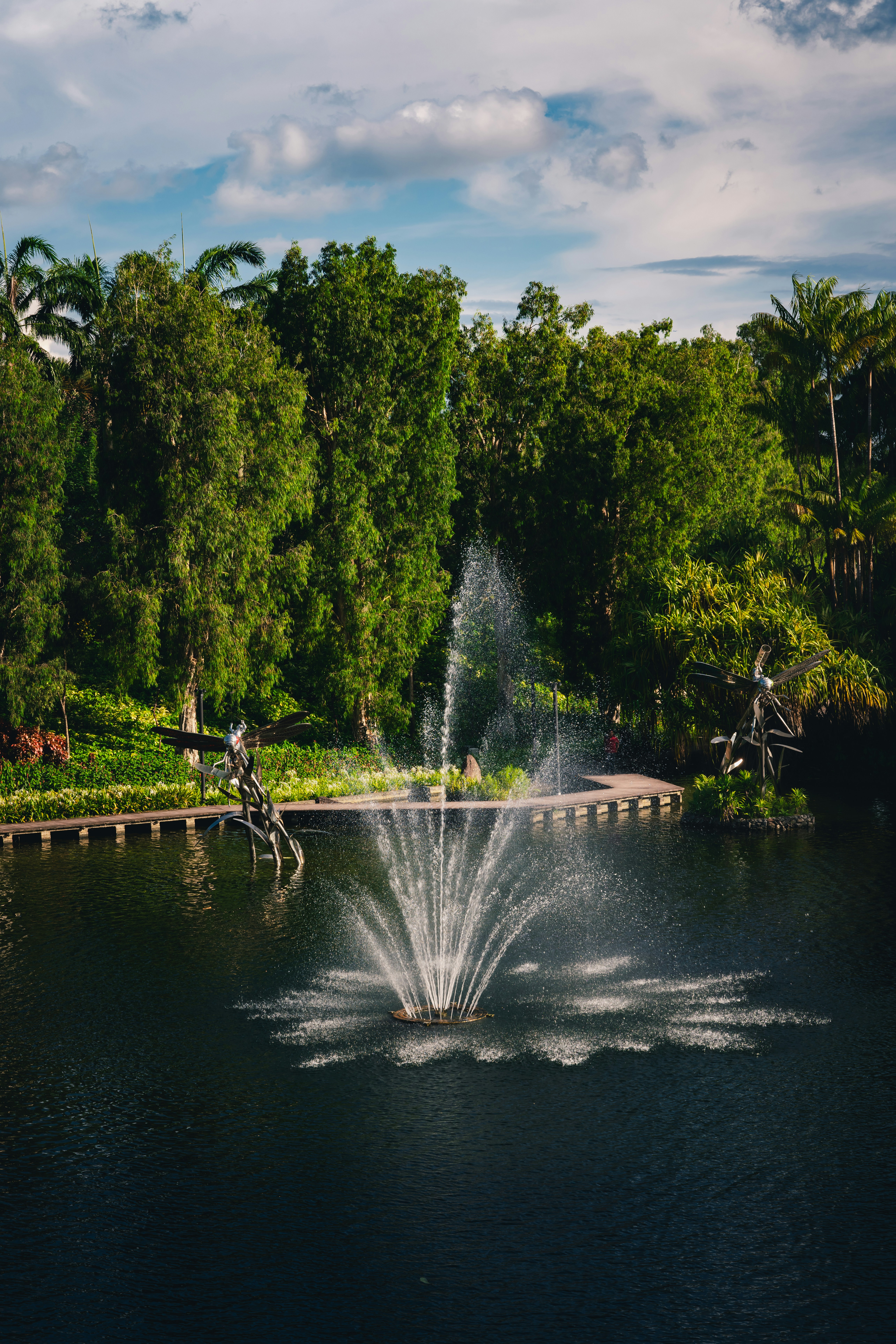 Fountain sprays water in a pond surrounded by trees.