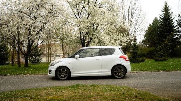 White car parked on a road with blooming trees.