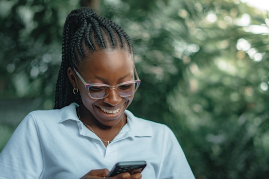 Woman with glasses smiles while looking at her phone.