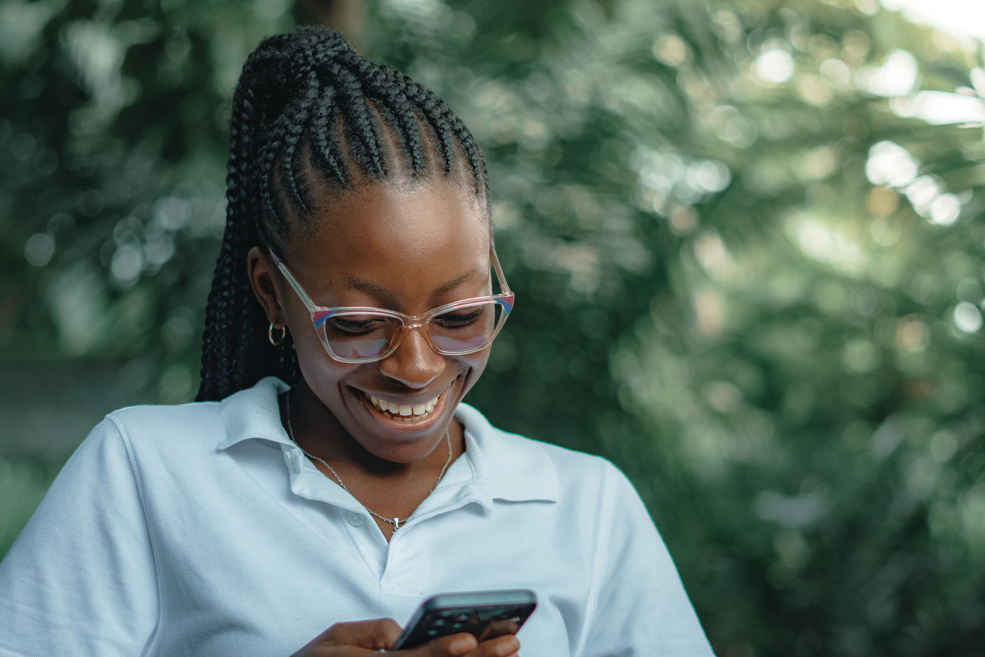 Woman with glasses smiles while looking at her phone.
