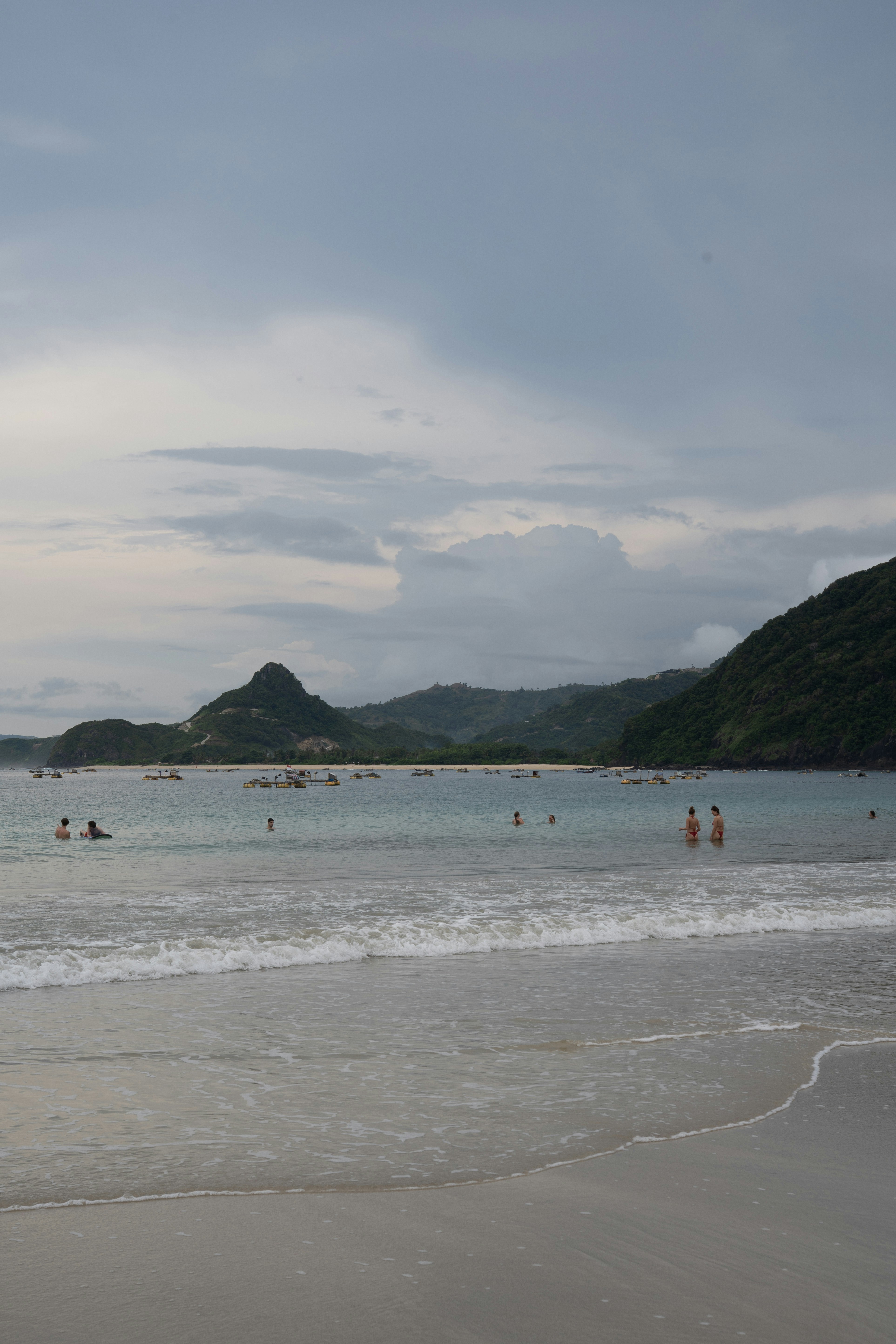 People enjoy the beach with mountains in the background.