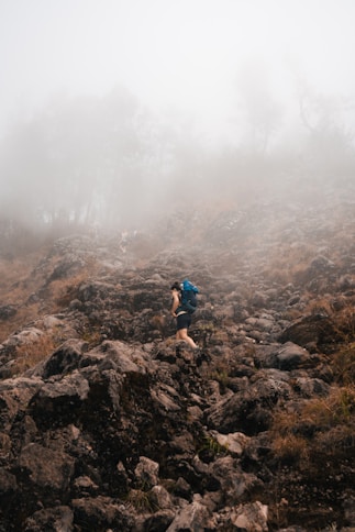 Hiker climbs a rocky mountain in foggy conditions.