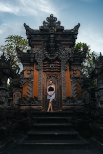 Woman stands in front of ornate temple doors.