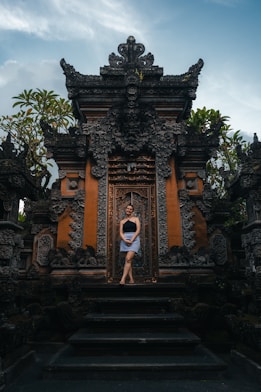Woman stands in front of ornate temple doors.
