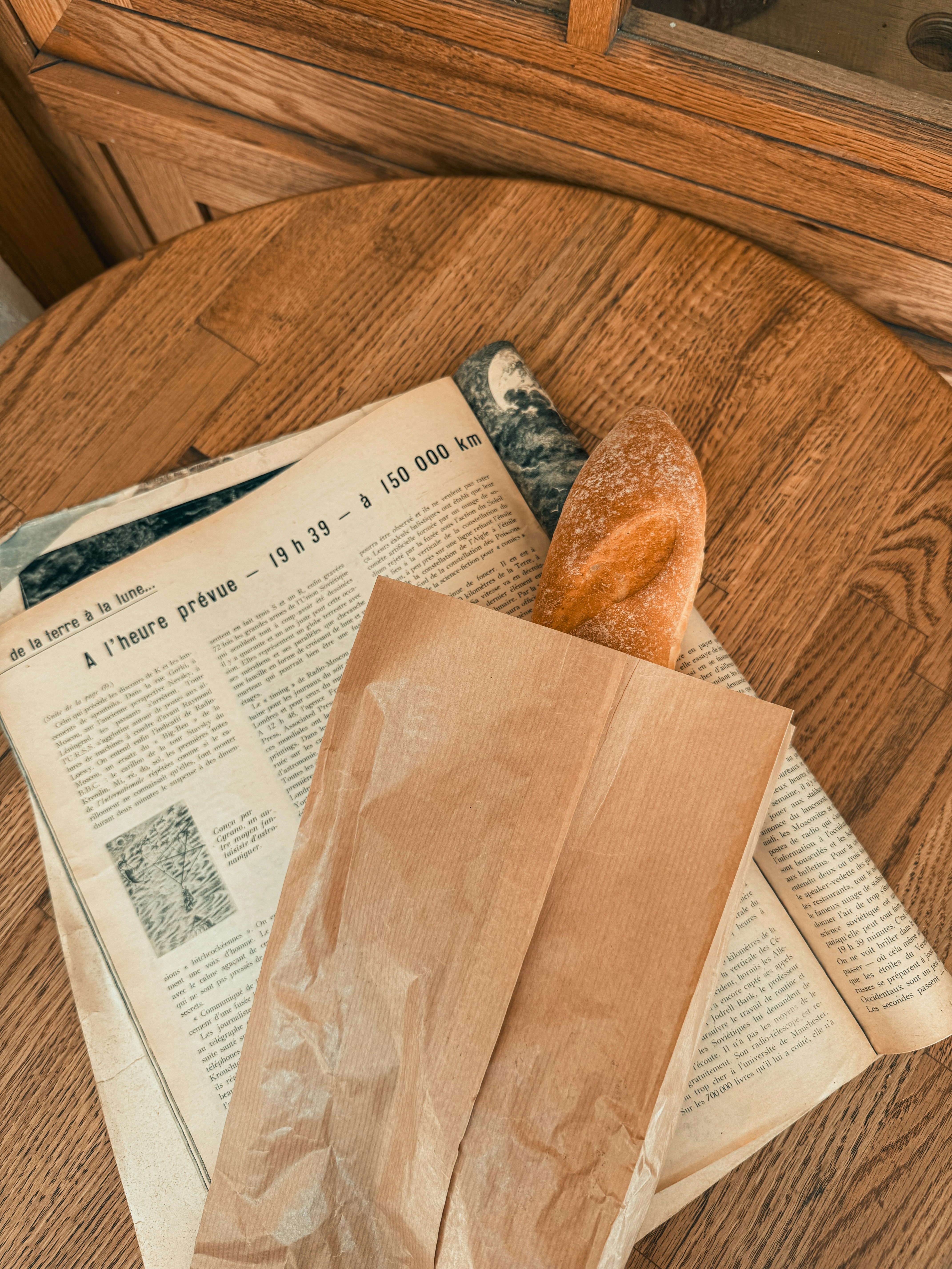A baguette rests with a newspaper on a table.