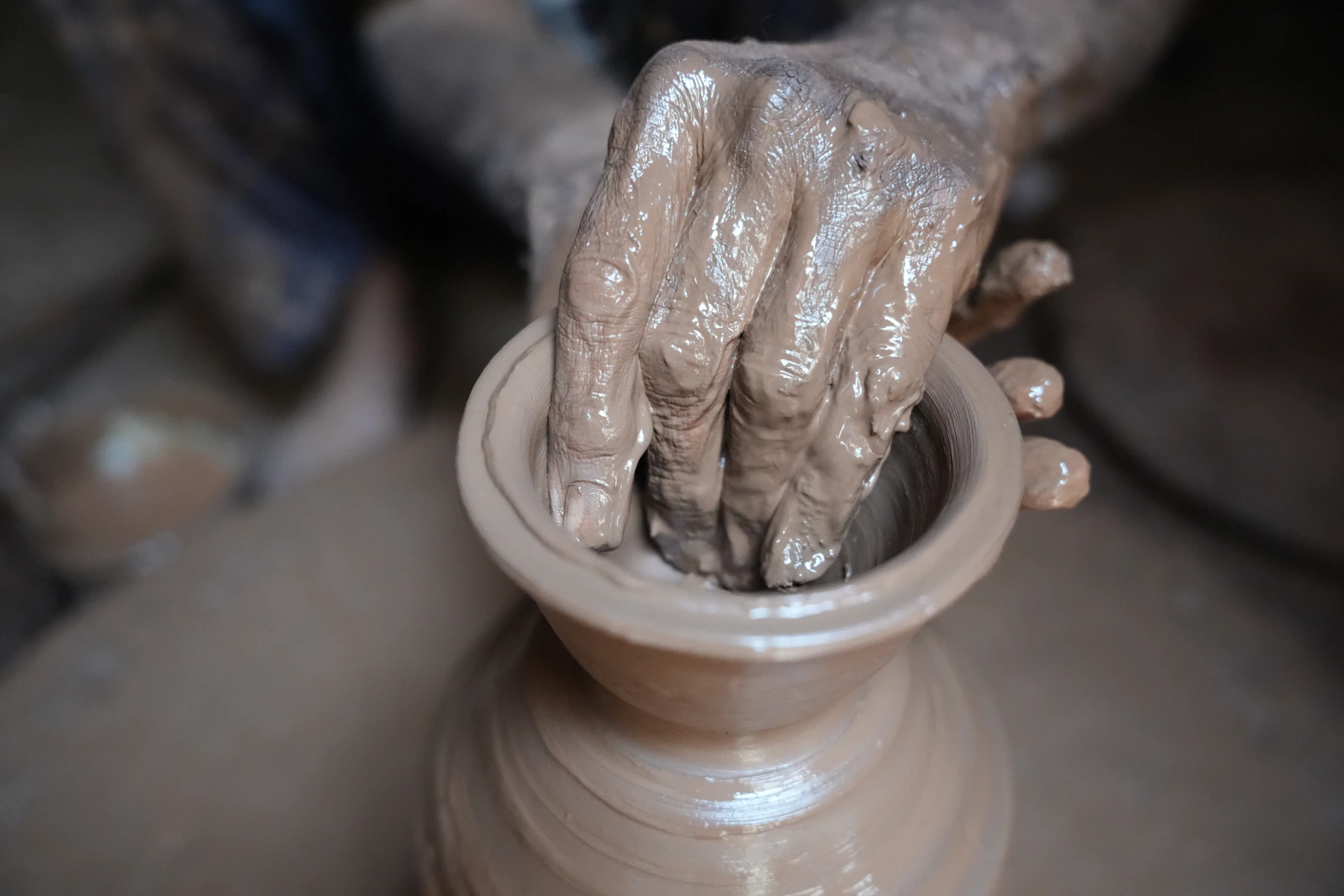 A potter shaping warm red terracotta clay by hand