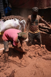 Workers are handling mud in a dusty environment.