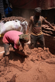 Workers are handling mud in a dusty environment.