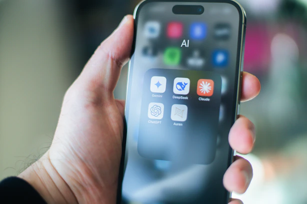 A hand holds a smartphone with various apps.