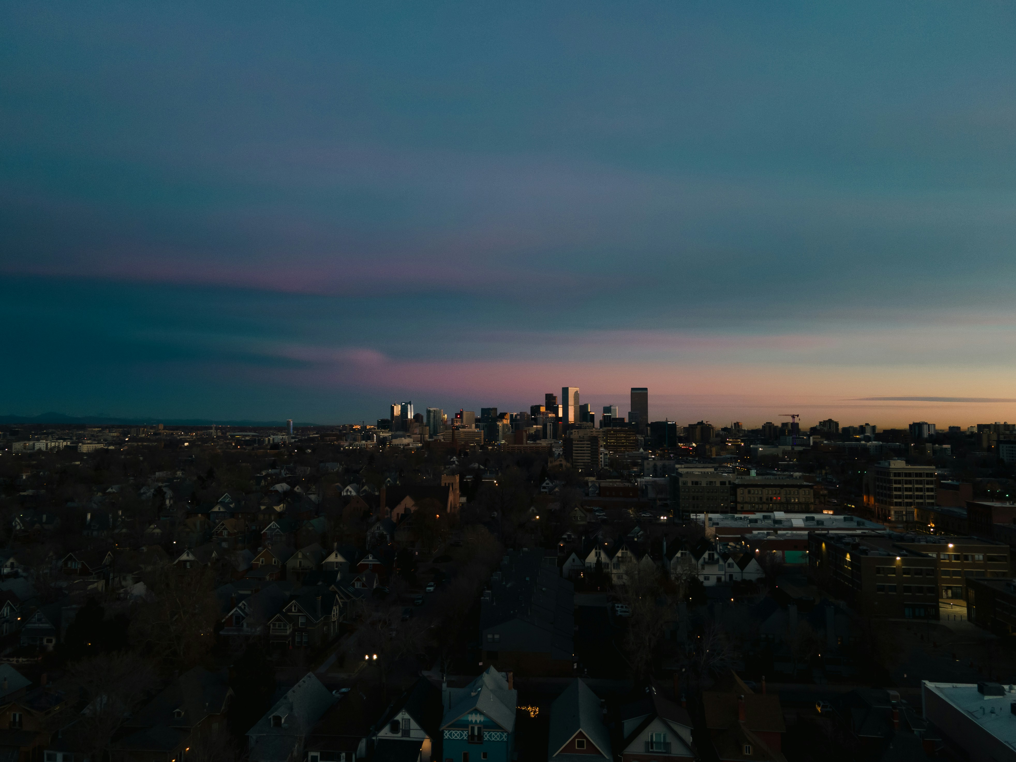Illuminated city skyscrapers rise above a dark residential neighborhood.